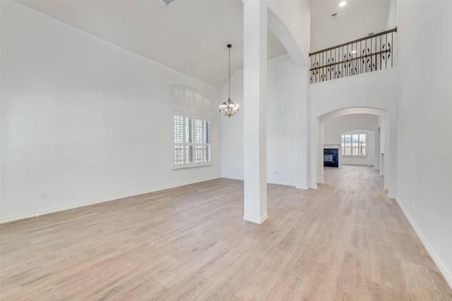 unfurnished living room featuring a wealth of natural light, a notable chandelier, a towering ceiling, and light wood finished floors