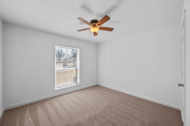 carpeted empty room with a textured ceiling, a ceiling fan, and baseboards