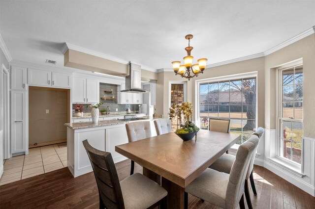 dining area featuring hardwood / wood-style floors, crown molding, visible vents, and a notable chandelier