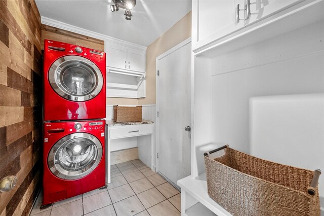 washroom with cabinet space, wooden walls, stacked washer / drying machine, and light tile patterned flooring