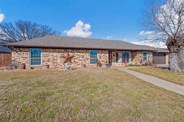 ranch-style home with brick siding, an attached garage, a front lawn, and roof with shingles