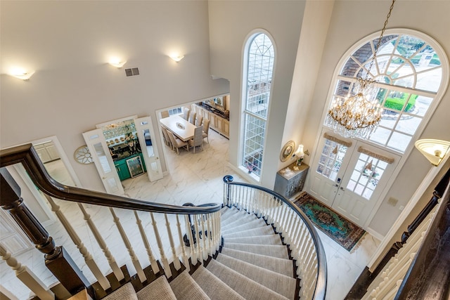 entrance foyer with french doors, visible vents, a towering ceiling, a chandelier, and stairs