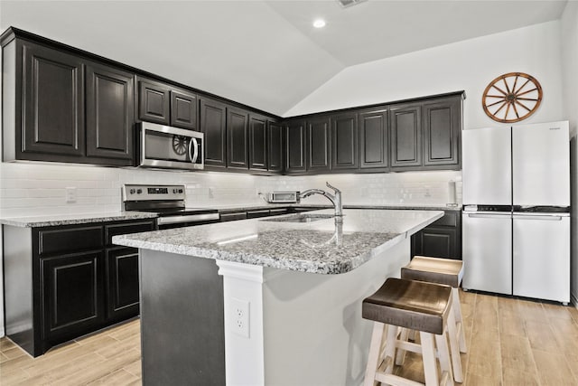 kitchen with lofted ceiling, a kitchen island with sink, stainless steel appliances, a kitchen breakfast bar, and light wood finished floors