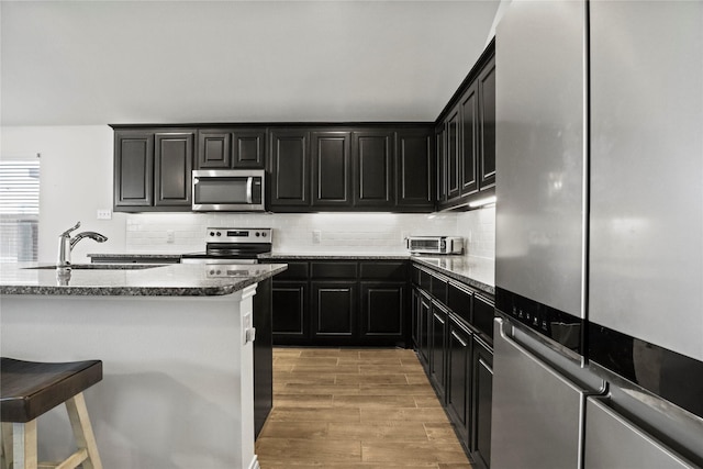 kitchen featuring appliances with stainless steel finishes, dark stone countertops, dark cabinetry, and a kitchen breakfast bar