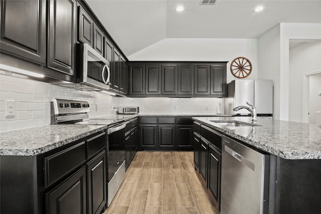 kitchen with an island with sink, dark cabinetry, appliances with stainless steel finishes, and a sink