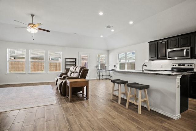 kitchen with a center island with sink, appliances with stainless steel finishes, a breakfast bar, open floor plan, and dark cabinets