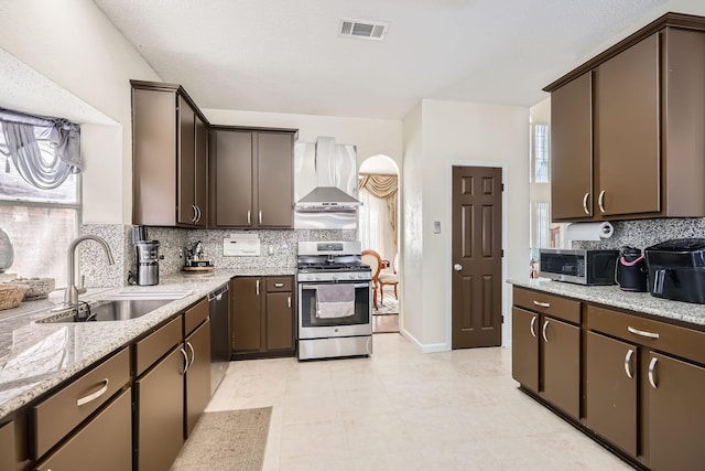 kitchen featuring a sink, visible vents, dark brown cabinets, appliances with stainless steel finishes, and wall chimney exhaust hood