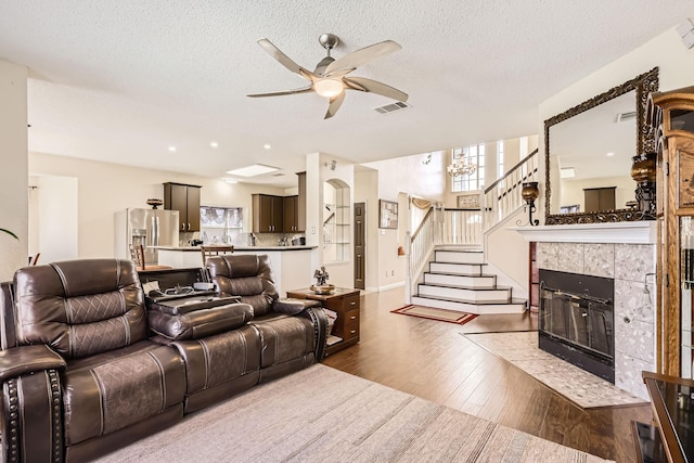 living room with dark wood-type flooring, a fireplace, visible vents, a ceiling fan, and stairs