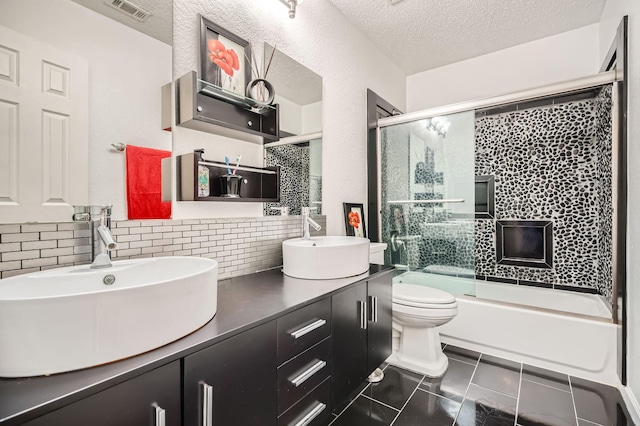 bathroom featuring a textured ceiling, toilet, bath / shower combo with glass door, a sink, and visible vents