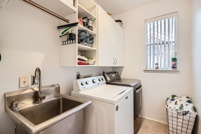 washroom with cabinet space, light tile patterned floors, baseboards, washing machine and clothes dryer, and a sink