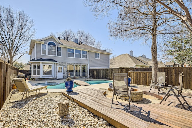 rear view of property with an outdoor fire pit, a fenced backyard, a wooden deck, a fenced in pool, and a patio area