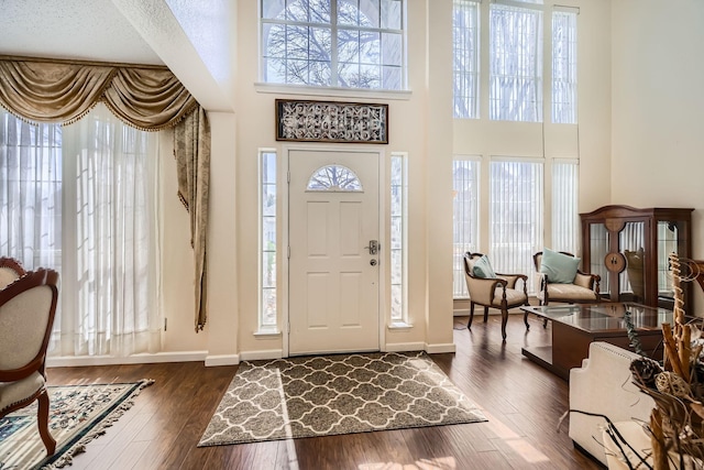 foyer entrance with a towering ceiling, dark wood-style floors, and baseboards