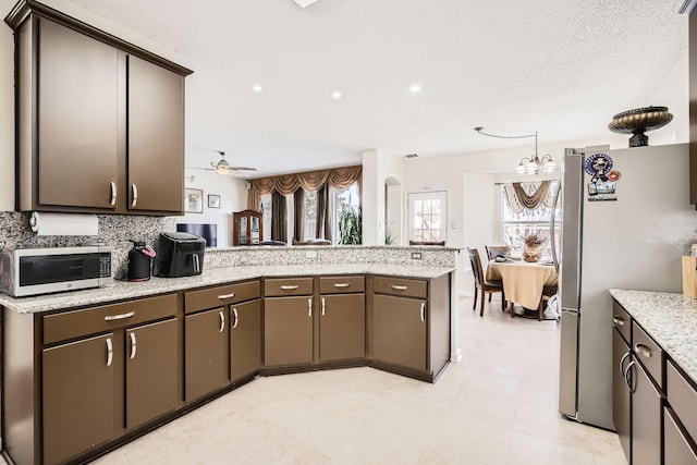 kitchen featuring ceiling fan with notable chandelier, a peninsula, appliances with stainless steel finishes, and dark brown cabinets