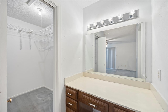 bathroom with a ceiling fan, a walk in closet, a textured ceiling, and vanity