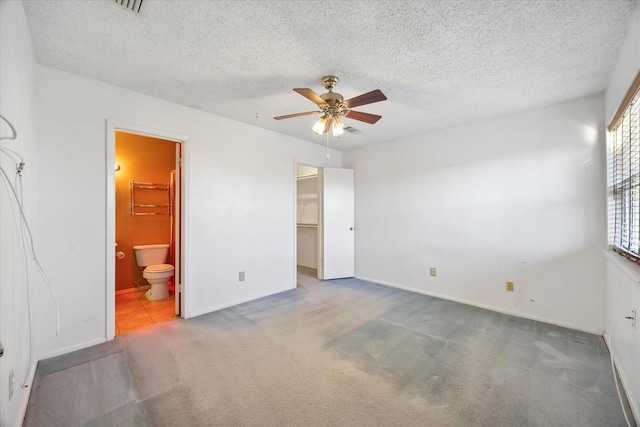 unfurnished bedroom featuring a textured ceiling, connected bathroom, a ceiling fan, carpet, and a walk in closet