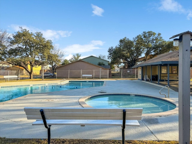 pool with a patio, fence, and a hot tub