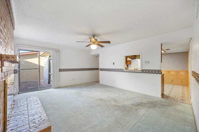 unfurnished living room featuring light carpet, visible vents, wainscoting, ceiling fan, and a textured ceiling