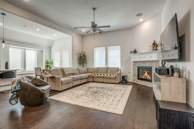 living area featuring dark wood-style flooring, ceiling fan, a stone fireplace, and a healthy amount of sunlight