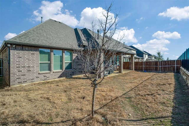 back of property featuring a shingled roof, a yard, a fenced backyard, and brick siding