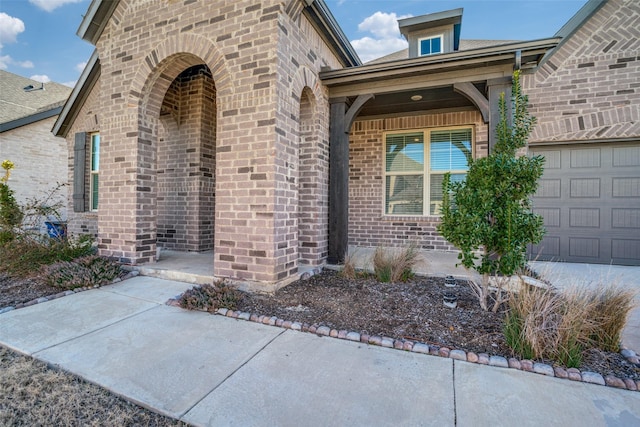 view of exterior entry with an attached garage and brick siding