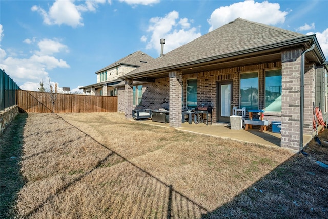 rear view of house featuring a patio, a fenced backyard, brick siding, roof with shingles, and a lawn