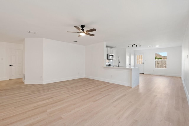 unfurnished living room with baseboards, visible vents, a sink, and light wood finished floors