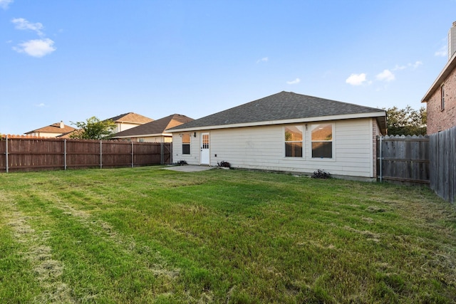 back of house featuring roof with shingles, a lawn, a patio area, and a fenced backyard