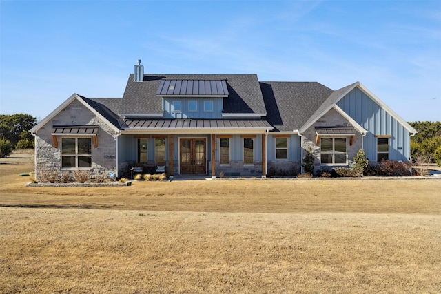 view of front facade with metal roof, stone siding, board and batten siding, a standing seam roof, and a chimney