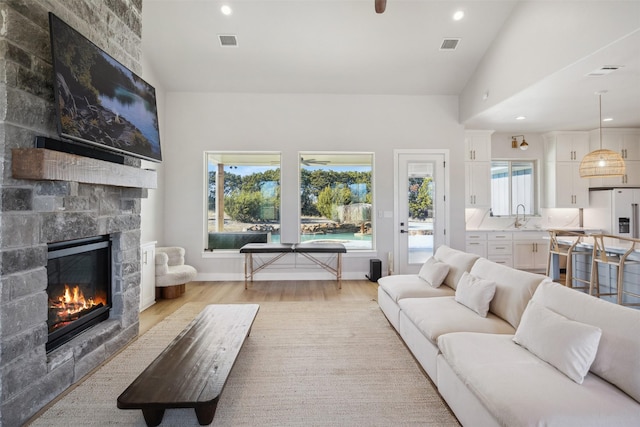 living room featuring light wood finished floors, a stone fireplace, visible vents, and recessed lighting