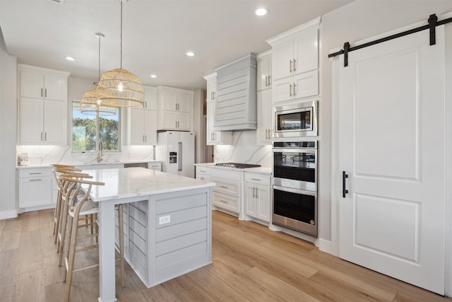 kitchen with a barn door, tasteful backsplash, appliances with stainless steel finishes, white cabinetry, and a sink