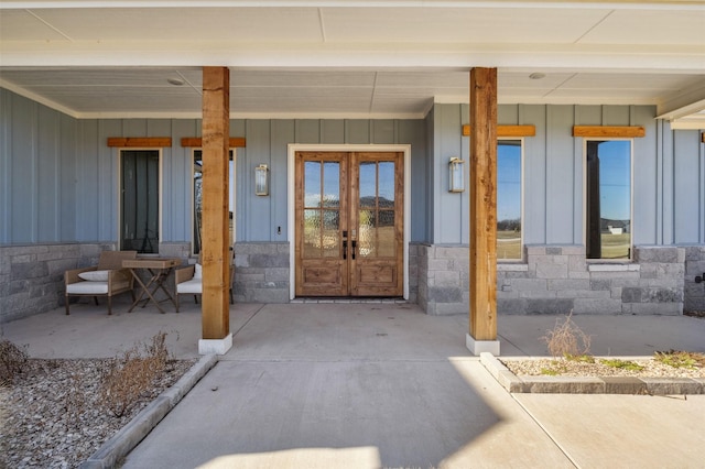 property entrance featuring board and batten siding, french doors, covered porch, and stone siding