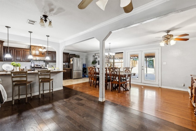 dining space with ceiling fan with notable chandelier, ornamental molding, dark wood-style flooring, and visible vents