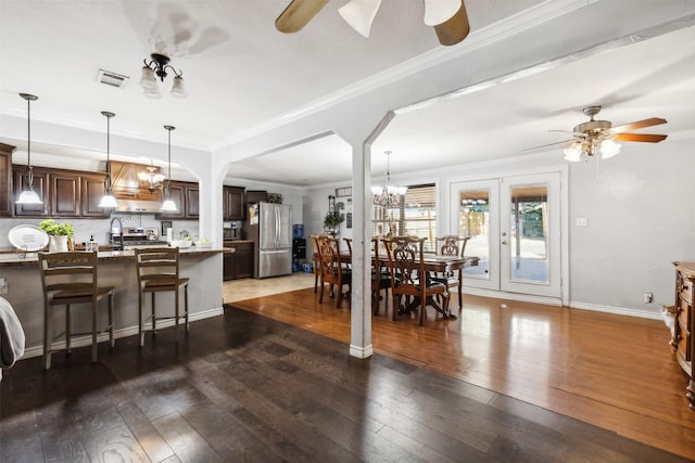 dining space with dark wood-style floors, ornamental molding, ceiling fan with notable chandelier, and visible vents