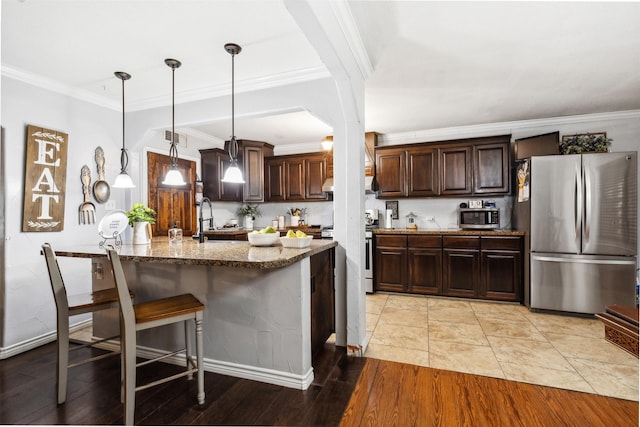 kitchen with stainless steel appliances, visible vents, hanging light fixtures, dark brown cabinets, and light stone countertops