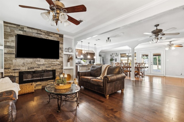 living area with a stone fireplace, hardwood / wood-style flooring, ceiling fan with notable chandelier, visible vents, and ornamental molding