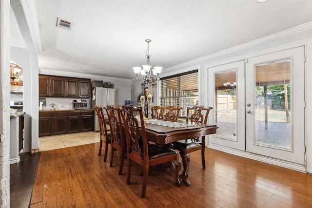 dining area featuring ornamental molding, visible vents, light wood-style flooring, and an inviting chandelier