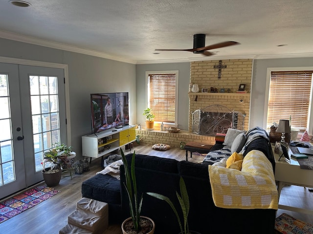 living room with french doors, a fireplace, light wood-style floors, ornamental molding, and a textured ceiling