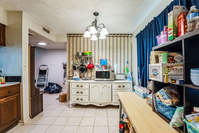 kitchen featuring stainless steel microwave, hanging light fixtures, visible vents, light tile patterned flooring, and a textured ceiling