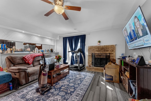 living area featuring ceiling fan, a fireplace, and wood finished floors