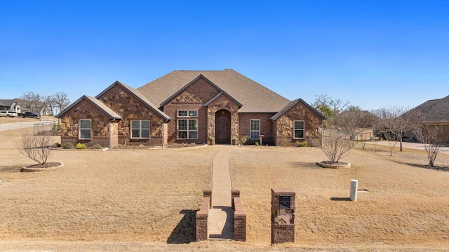 view of front facade with a shingled roof, stone siding, brick siding, and fence