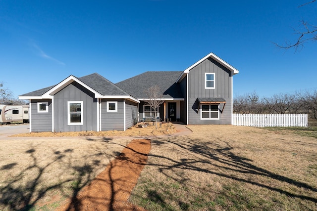 view of front of home featuring roof with shingles, board and batten siding, a front yard, and fence