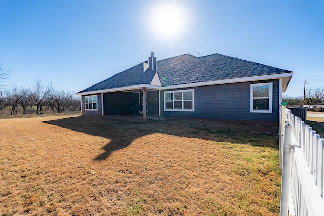 back of property with roof with shingles, a chimney, fence, and a yard