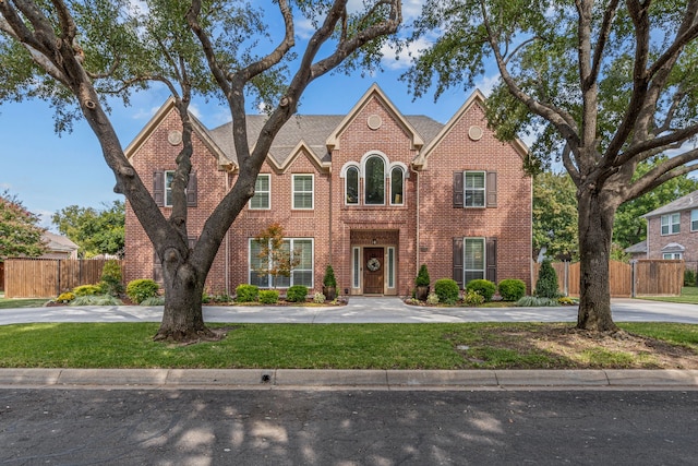 view of front facade featuring driveway, a front yard, fence, and brick siding