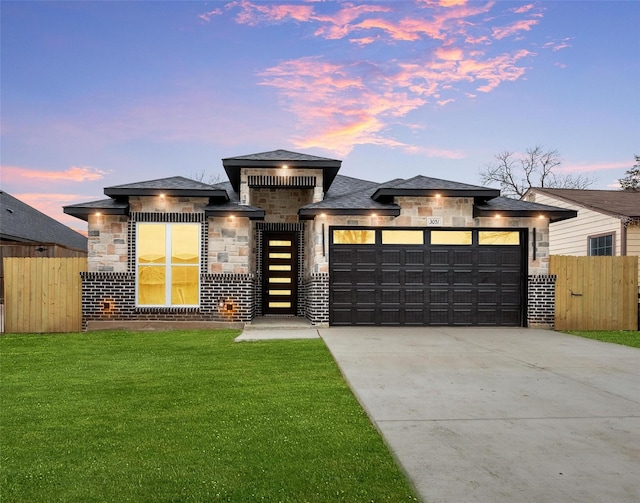 prairie-style house with driveway, a garage, stone siding, fence, and a yard