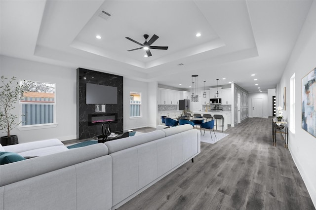 living area with light wood-style floors, a tray ceiling, visible vents, and a premium fireplace