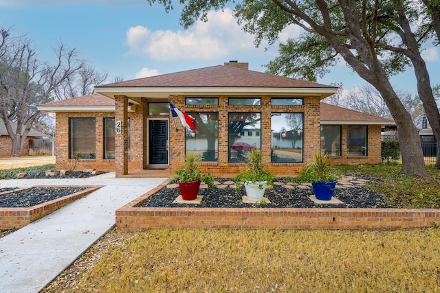 view of front facade featuring a shingled roof, a front yard, a chimney, and brick siding