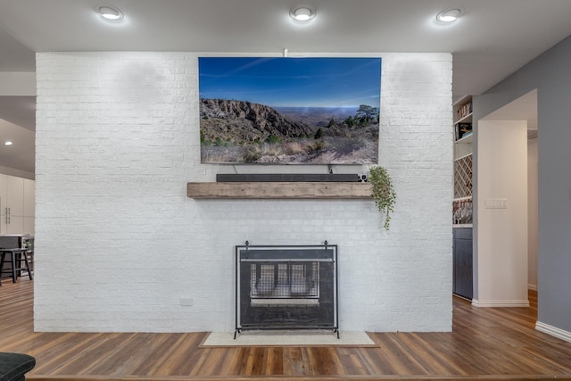 details featuring a brick fireplace, wood finished floors, and recessed lighting