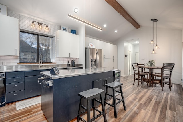 kitchen with white cabinets, a kitchen island, a breakfast bar area, hanging light fixtures, and stainless steel refrigerator with ice dispenser