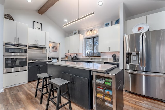 kitchen with a kitchen island, wine cooler, vaulted ceiling with beams, stainless steel appliances, and white cabinetry