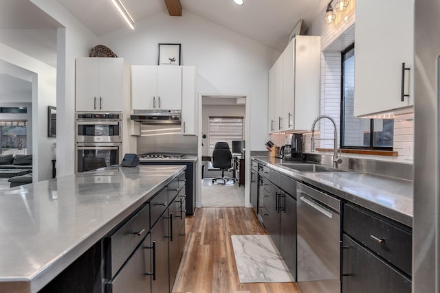 kitchen with stainless steel appliances, stainless steel countertops, a sink, and white cabinetry